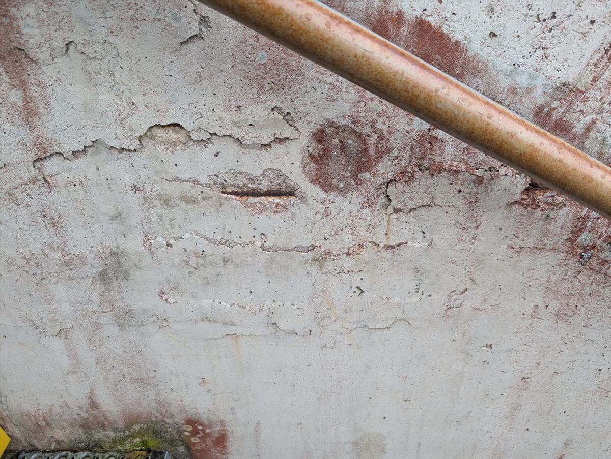 Béton éclaté, aciers apparents : sous-face de dalle avec béton éclaté, armatures à nu et corrodées, coulures de rouille.